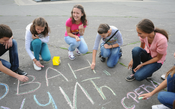 Six young people in a circle drawing on the ground with chalk.