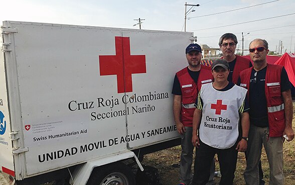 Three members of the Swiss Humanitarian Aid Unit and an Ecuadorian Red Cross worker stand in front of a trailer transporting drinking water.