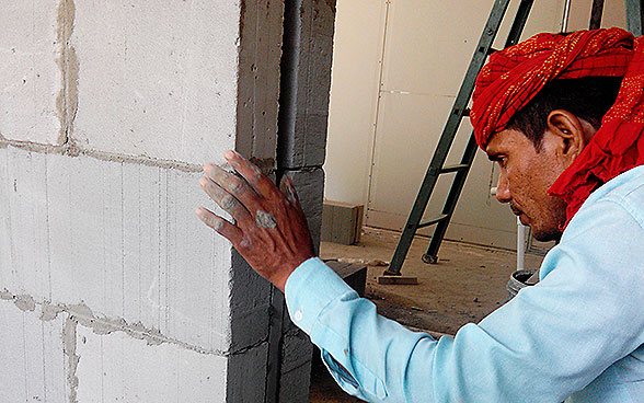 Un ouvrier indien érige un mur avec des blocs de ciment LC3. 