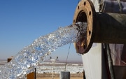 Water flowing out of a pipe with the Azraq refugee camp in the background.
