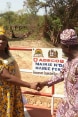 Una mujer estrechándole la mano a un hombre frente a un cartel con el logo de Suiza y el nombre de dos municipios que participaron en la construcción del puente.