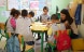 Klassenzimmer mit einer Lehrerin, die vor einer Gruppe von Schülerinnen und Schülern sitzt und ein Buch zeigt.