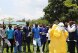 a group of health workers listen to the trainer's instructions, assisted by two individuals wearing protective clothing.   