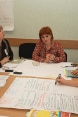 Women holding a discussion around a table covered in notebooks and brochures.