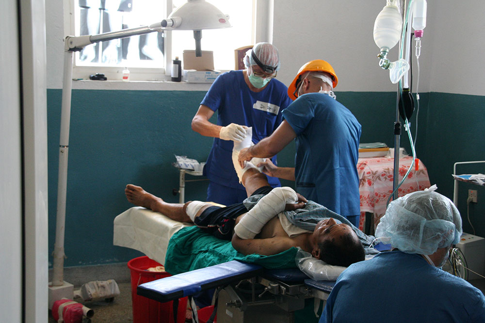 Tre medici operano una gamba di un ferito in Nepal.  
