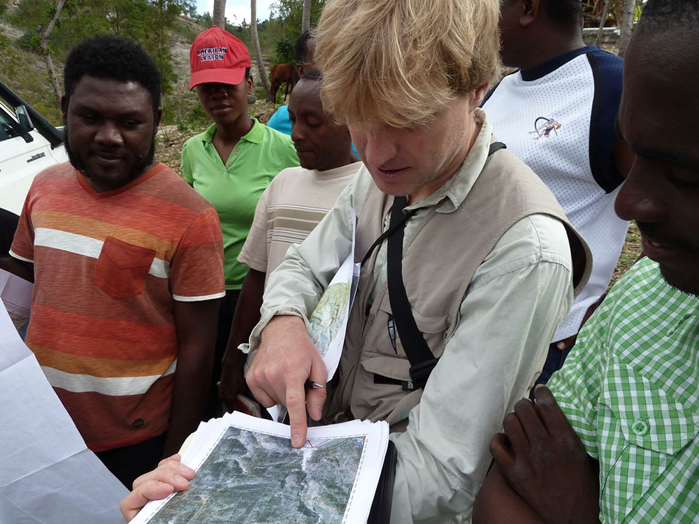 Un esperto svizzero, attorniato da esperti haitiani, indica un punto su una carta con un dito.  