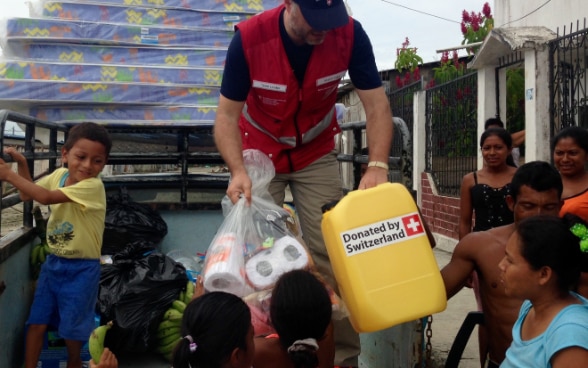 Un expert suisse tend un bidon d’eau potable à des enfants depuis une camionnette. 