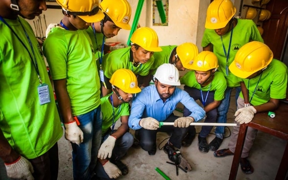 An instructor shows a group of men wearing hard hats how plastic pipes are processed.