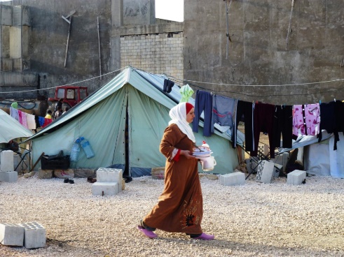 A woman refugee walks in front of a tent. 