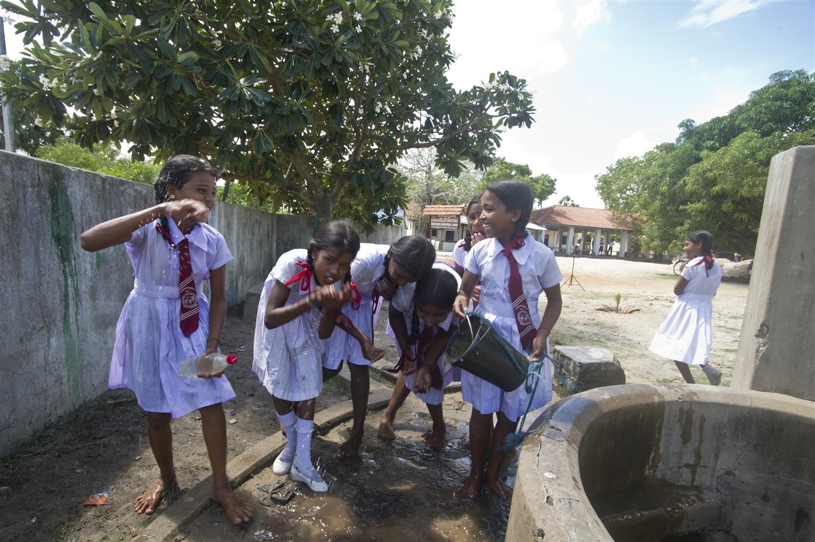 Schülerinnen trinken Wasser an einem neuen Brunnen.