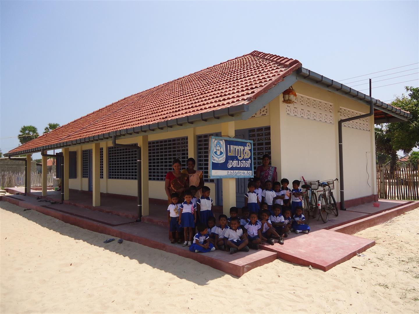 Eine Gruppe von Kindern posiert mit Lehrerinnen vor einem neuen Schulgebäude.