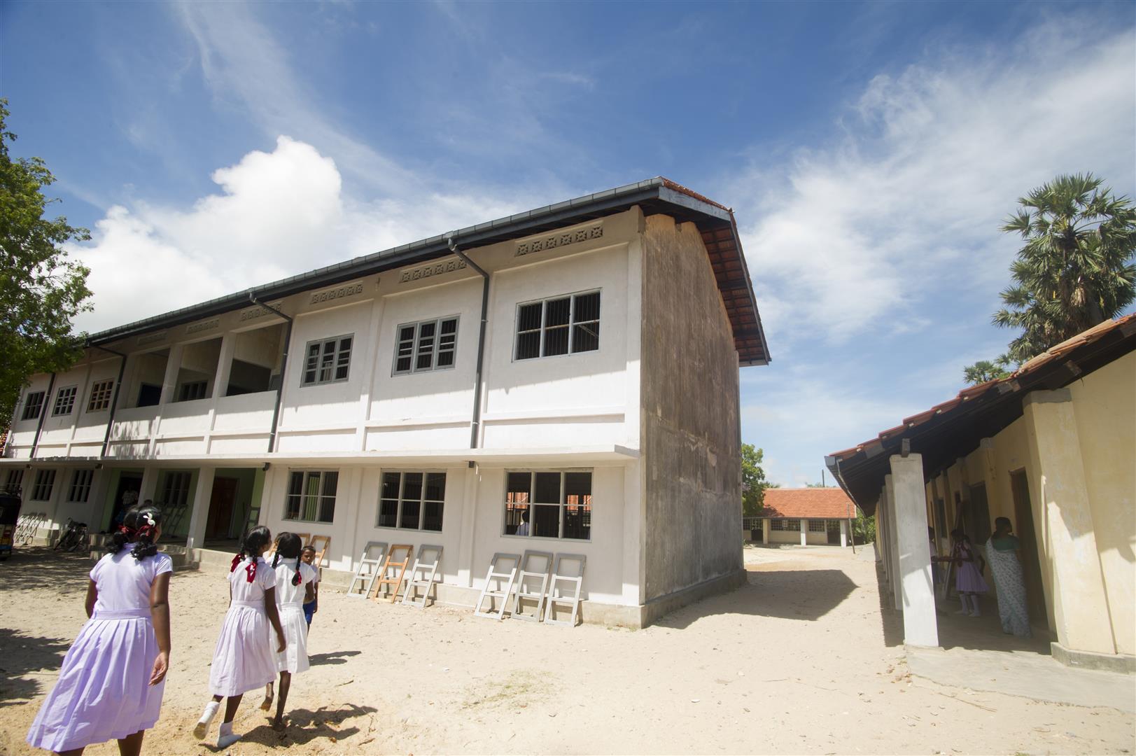 Drei Schülerinnen laufen auf ein zweistöckiges Schulgebäude zu.