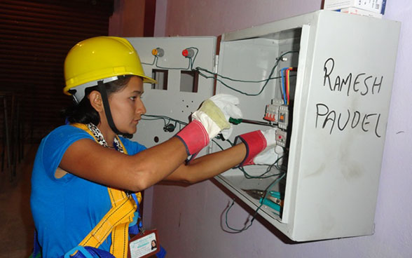 Una aprendiz maneja un destornillador en un tablero eléctrico