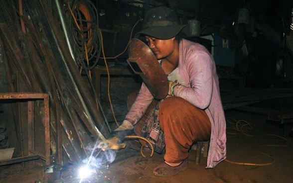 Una aprendiz suelda un trozo de metal, provista de una máscara de protección