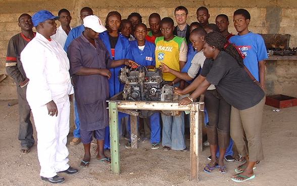 Au Burkina Faso, des femmes et des hommes se tiennent autour d’une table sur laquelle est posée une machine.