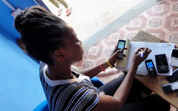 Una mujer africana se sienta en una mesa en la que varios teléfonos móviles están acostados y transfiere números a una mesa.