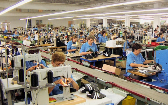 View into a factory building in Bosnia-Herzegovina, where numerous women sew shoes on sewing machines.