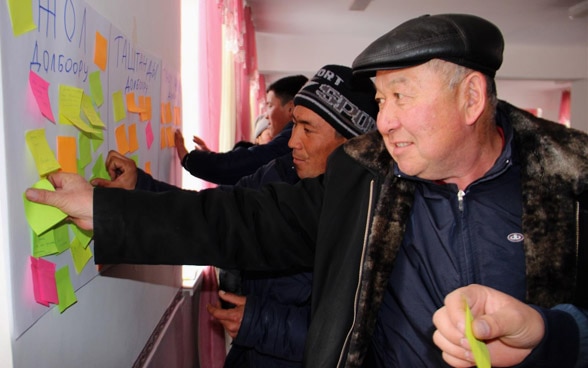 Männer stehen vor einer Wand mit Post-it Zetteln