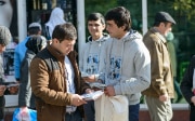 Deux jeunes hommes s’adressent à un passant auquel ils remettent une brochure informative.