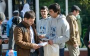 Two young men talk to a passer-by and hand him a leaflet.