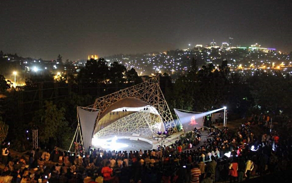The Genocide Memorial Centre in Kigali at night during Ubumuntu Arts Festival. The audience is watching an open-air performance. 