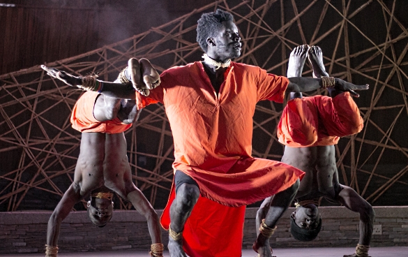 Three dancers performing at Ubumuntu Arts Festival. The dancer in the middle squats with outstretched arms. The dancers to the left and right of him are standing on their heads.