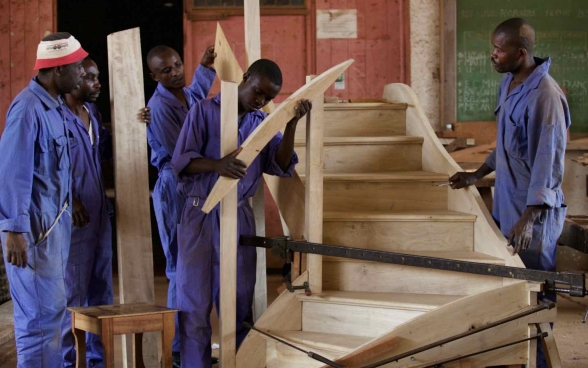 Eine Gruppe junger Schreiner in Ausbildung baut eine Holztreppe zusammen. 