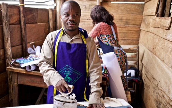 A man irons a piece of fabric on a wooden table.
