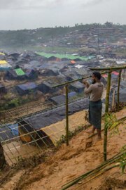 A man stands on the edge of a refugee camp in Cox’s Bazar. He is building a shelter for his family out of lengths of wooden pole.