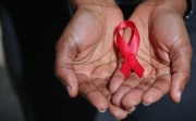 Hände halten ein Band, welches das AIDS-Symbol darstellt.