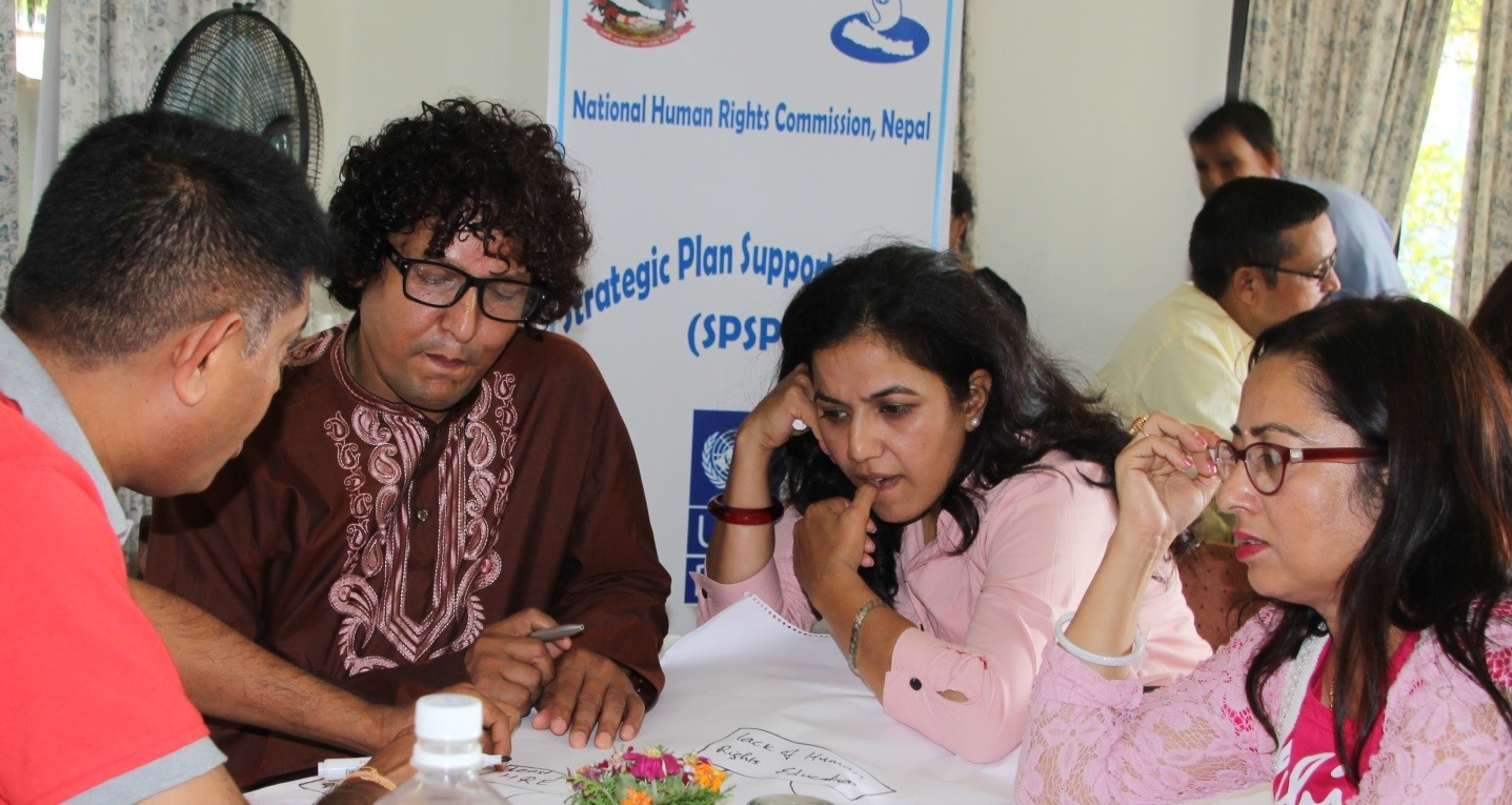 Two women and two men sit talking around a table.   They are thinking and writing on a sheet of paper from a flip chart.