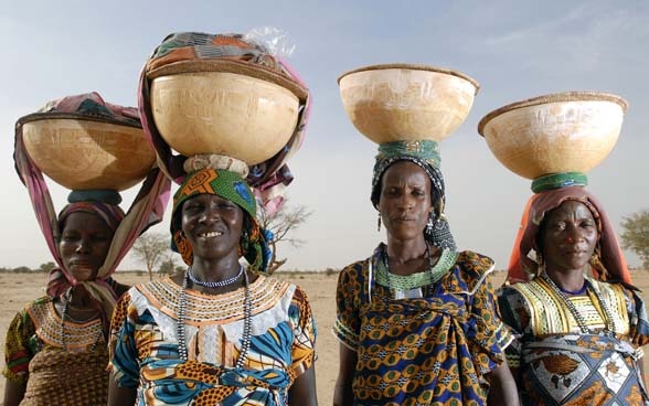 Vier Frauen mit Körben voller Getreide auf dem Kopf. 