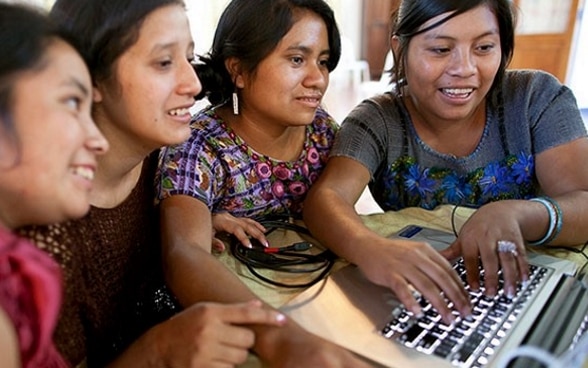 Vier Frauen sitzen vergnügt vor einem Laptop und arbeiten.