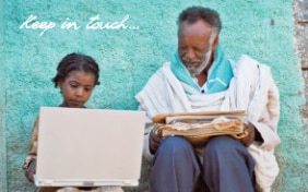 Une jeune fille africaine tenant un ordinateur portable et un vieil homme tenant des journaux, assis à côté de l'autre.