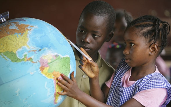 Des enfants regardent un globe terrestre dans une classe d'école.