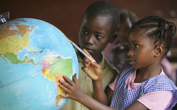 Bambini in classe che guardano un mappamondo. 