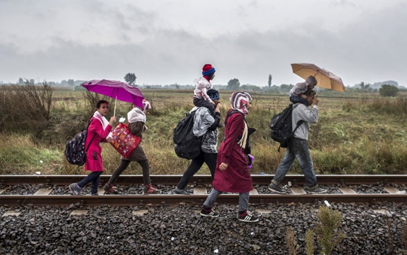 Refugees walking along rail tracks in the rain.