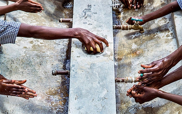 A picture of people's hands underneath water taps