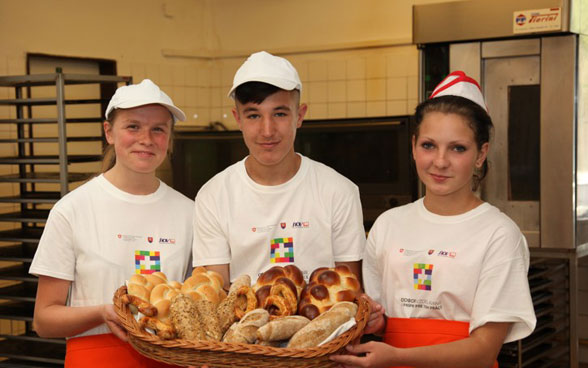 Trois jeunes apprentis boulangers montrent les pains qu'ils ont confectionnés.
