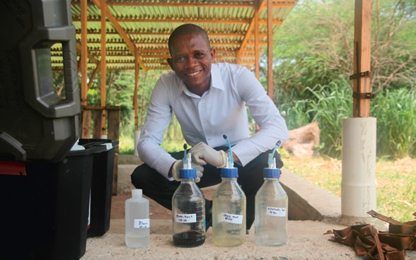 An expert crouching in front of laboratory vials containing product samples being tested in Haiti.