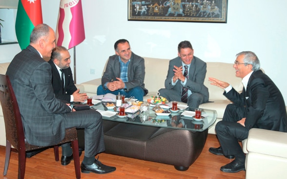 Fünf Männer diskutieren während eines offiziellen Treffens an einem Tisch.