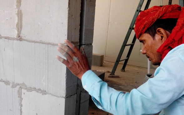 Un muratore lavora alla realizzazione di un muro in cemento.