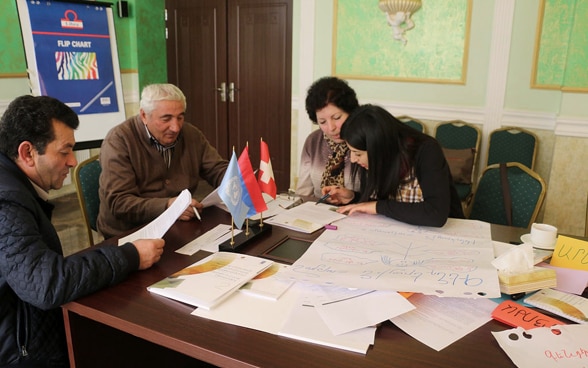 Zwei Männer und zwei Frauen studieren Akten in einem Sitzungsraum in Armenien.