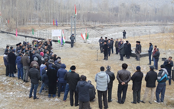 A crowd of around thirty people stand around a man giving a speech for the opening of an irrigation pipeline