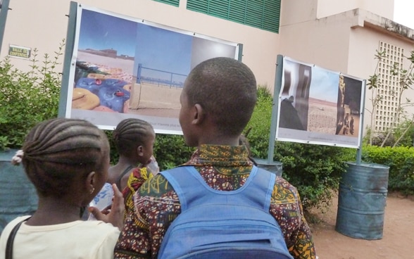Three children look at an outdoor photo exhibition.