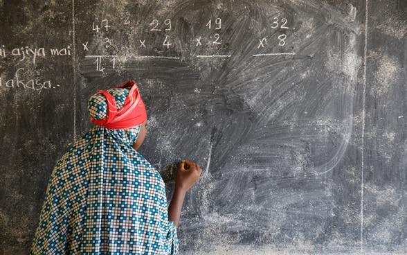 Ein Schulmädchen im Niger schreibt mit Kreide an die Wandtafel.
