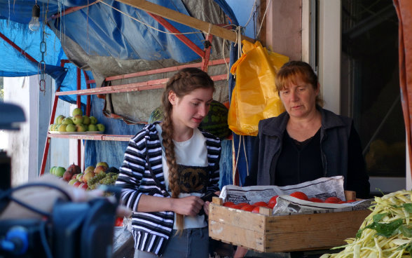 L’immagine mostra una venditrice al mercato di Senaki mentre pesa i pomodori portati da Medea e da suo padre.