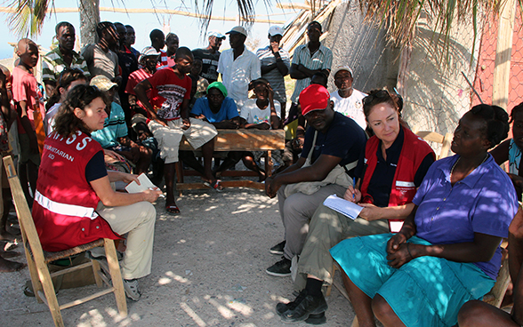 Two Swiss experts listen to a Haitian woman in the presence of other local people.
