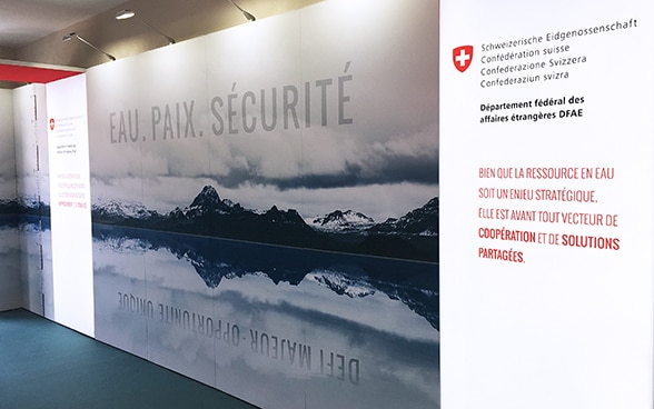 Un grande pannello che mostra un paesaggio di montagna e, in maiuscolo, le parole «ACQUA», «PACE» e «SICUREZZA».