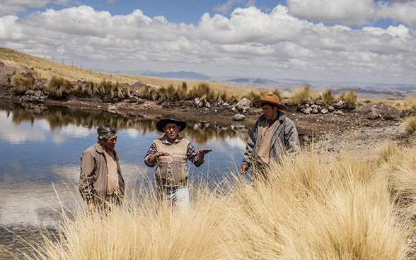 Three men stand talking by a reservoir.